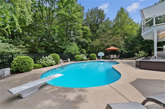View of pool featuring a patio, a fenced backyard, a diving board, and view of wooded area | Image 69