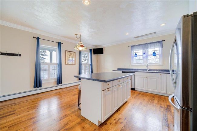 Kitchen featuring a sink, white cabinetry, stainless steel appliances, light wood-style flooring, and a baseboard heating unit | Image 13