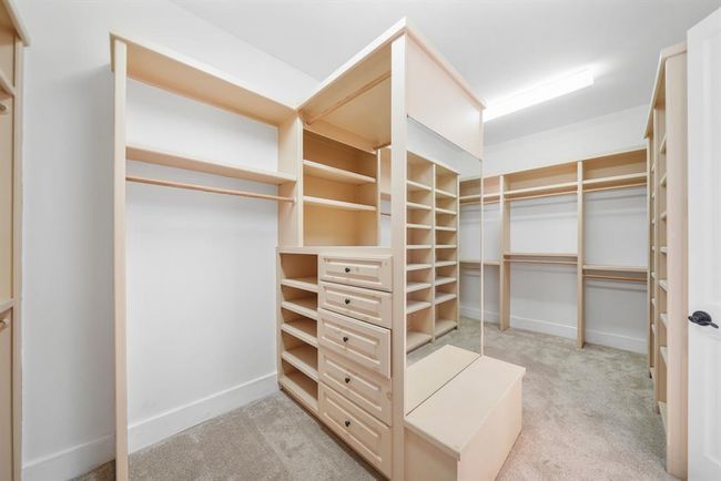 Need storage space? Included are two custom walk-in closets. This closet accessible from the private bath includes double-hung wardrobe storage rods, plenty of built-in storage shelves, a built-in dresser, wall mounted mirror with bench seating below & carpet. | Image 25