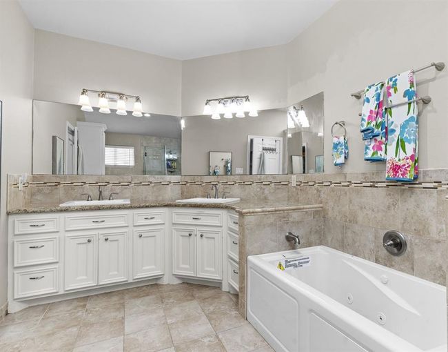 You're looking at a spacious bathroom featuring dual vanities with ample storage, a large mirror with bright lighting, and a luxurious built-in bathtub. The tile work and neutral color palette provide a serene, elegant atmosphere. | Image 32