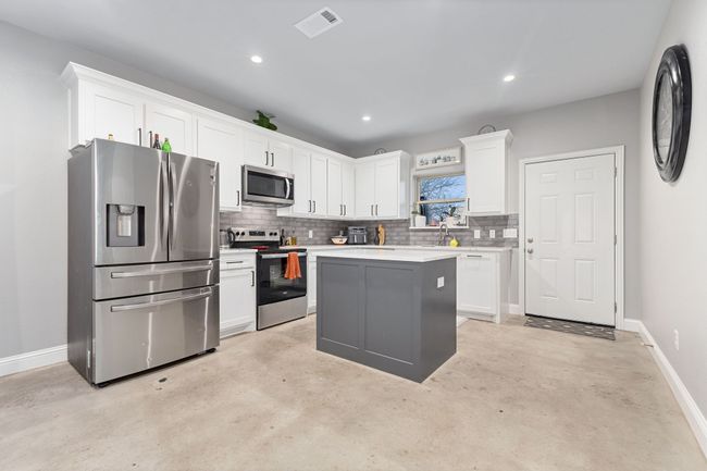 Kitchen with backsplash, stainless steel appliances, a center island, and white cabinets | Image 11