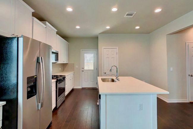 Kitchen with light countertops, visible vents, stainless steel appliances, a sink, and dark wood-style floors | Image 10