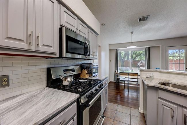Kitchen with appliances with stainless steel finishes, decorative backsplash, a textured ceiling, light stone counters, and gray cabinetry | Image 4