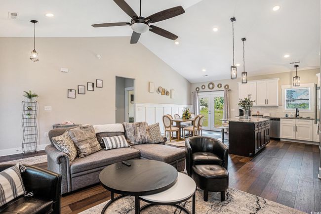 Living area with healthy amount of natural light, dark wood-style flooring, a ceiling fan, high vaulted ceiling, and french doors | Image 6