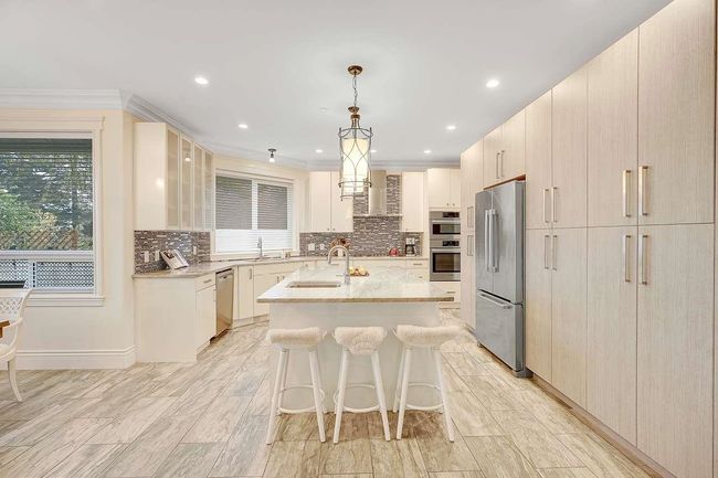 Kitchen featuring stainless steel appliances, an island with sink, light stone countertops, decorative backsplash, and a breakfast bar area | Image 7