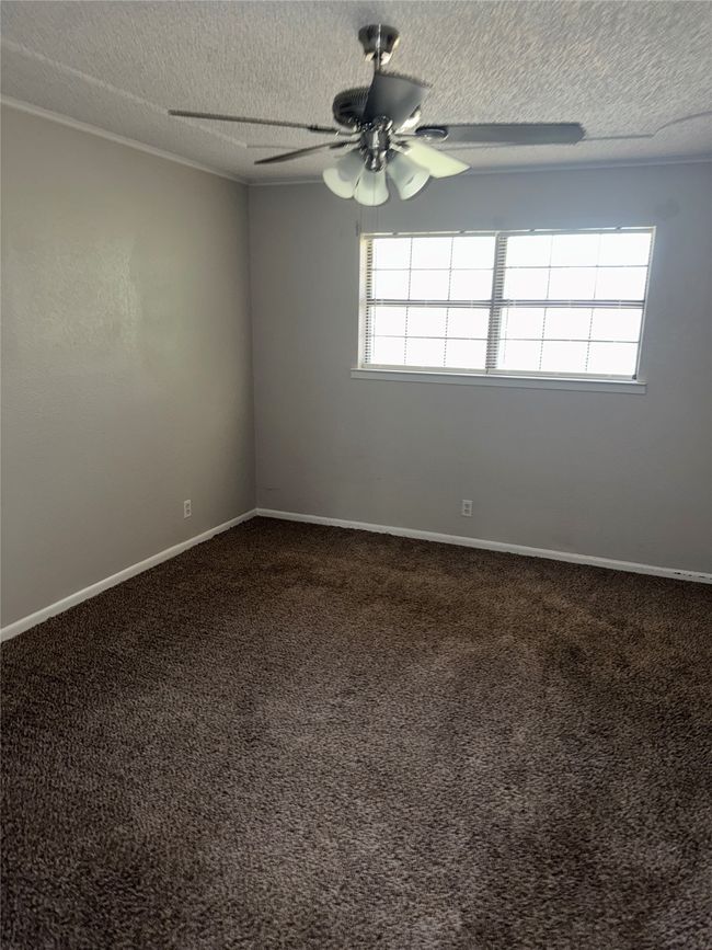 Unfurnished room with a ceiling fan, healthy amount of natural light, dark carpet, a textured ceiling, and baseboards | Image 12