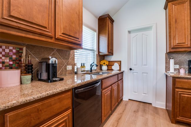 Kitchen with dishwashing machine, tasteful backsplash, light stone counters, light wood-style floors, and brown cabinetry | Image 4