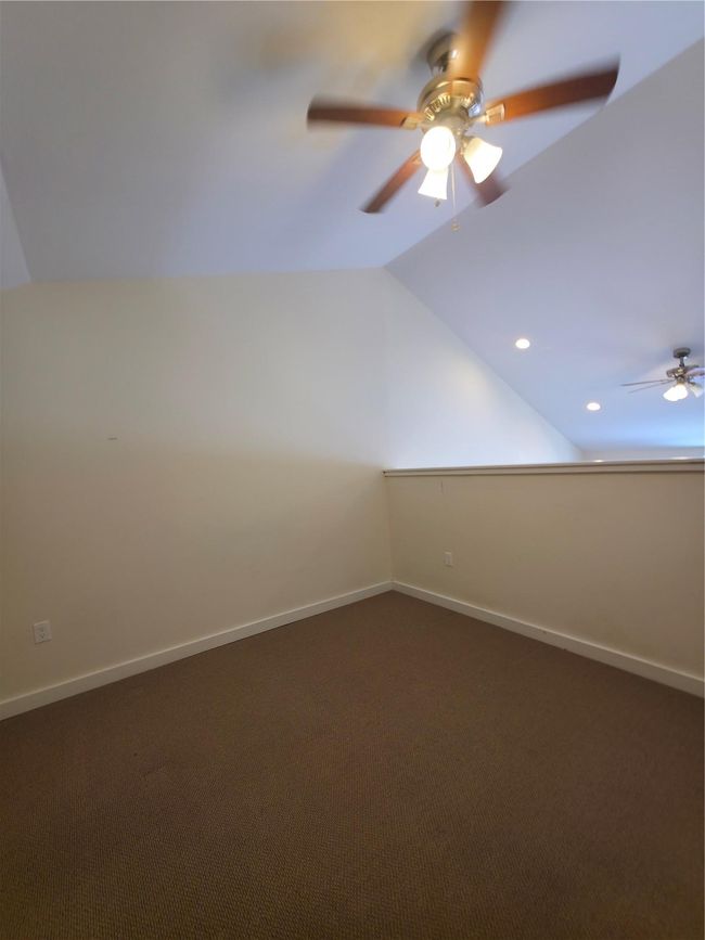 Empty room with lofted ceiling, ceiling fan, dark carpet, and baseboards | Image 16