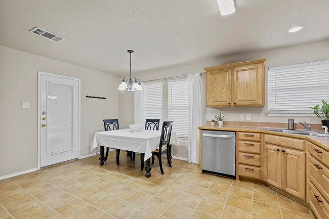 Kitchen featuring light brown cabinets, a sink, visible vents, stainless steel dishwasher, and decorative light fixtures | Image 17