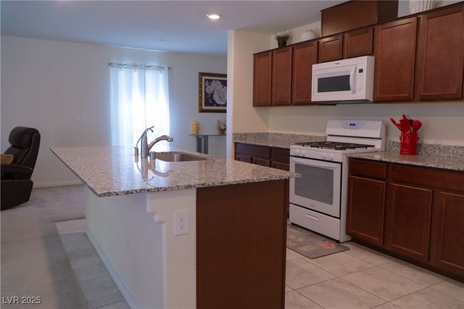 Kitchen with a sink, an island with sink, light stone counters, and white appliances | Image 23