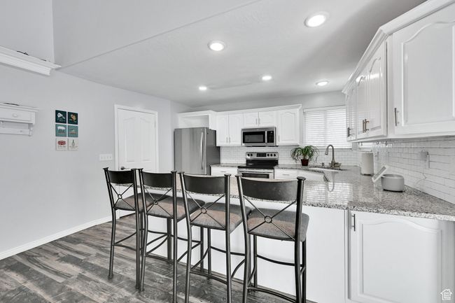 Kitchen featuring white cabinetry, baseboards, a sink, a peninsula, and appliances with stainless steel finishes | Image 13