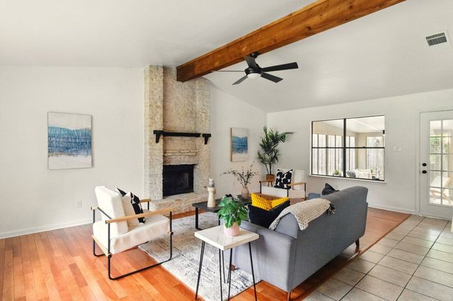 Open-concept living area with vaulted ceilings, a striking wooden beam, and a floor-to-ceiling stone fireplace. Refinished hardwood floors round out the living room space. | Image 4