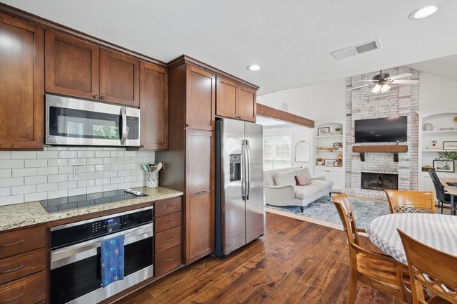 Kitchen with stainless steel appliances, open floor plan, dark wood finished floors, a fireplace, and light stone countertops | Image 9