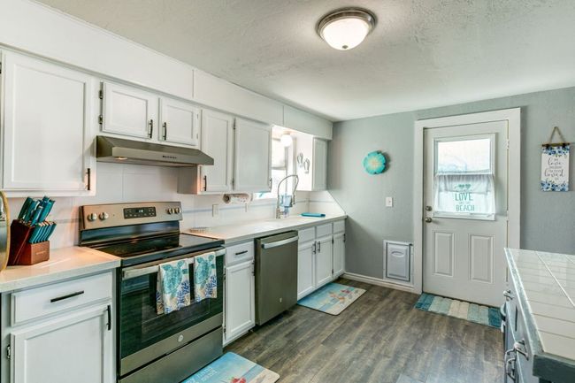 Kitchen with appliances with stainless steel finishes, a textured ceiling, under cabinet range hood, white cabinets, and dark wood-style flooring | Image 8