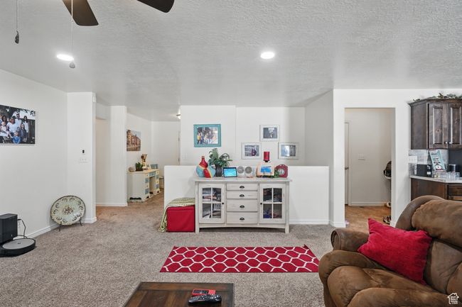 Living room with a textured ceiling, baseboards, a ceiling fan, and carpet floors | Image 13
