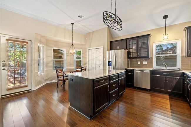 Kitchen featuring appliances with stainless steel finishes, decorative backsplash, glass insert cabinets, a sink, and dark wood-style flooring | Image 14