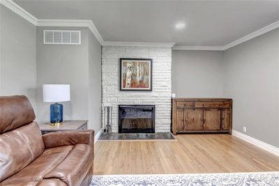 Living room featuring a stone fireplace, ornamental molding, and light wood-type flooring | Image 3