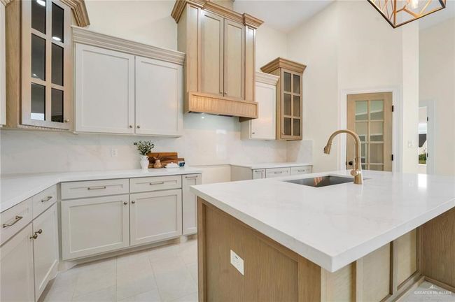 Kitchen featuring a sink, backsplash, glass insert cabinets, an island with sink, and light tile patterned floors | Image 11