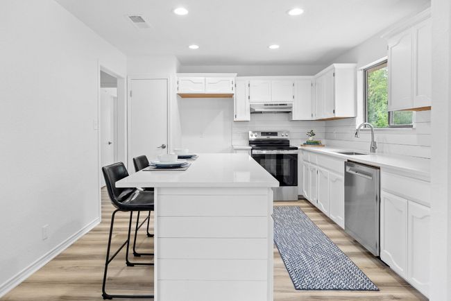 Kitchen featuring appliances with stainless steel finishes, under cabinet range hood, backsplash, recessed lighting, and white cabinets | Image 9
