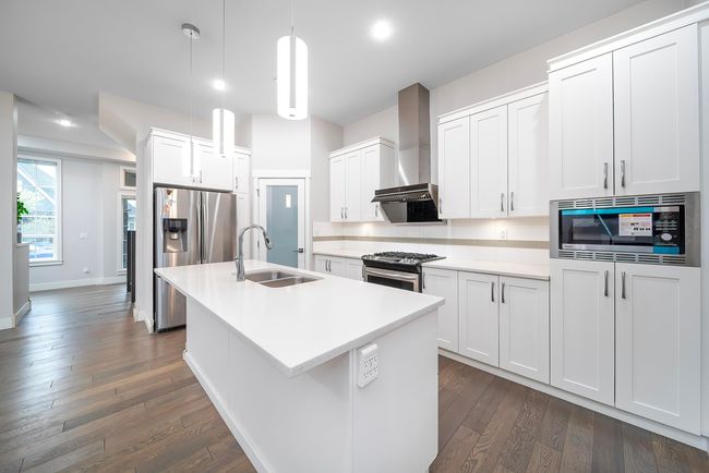Kitchen featuring a sink, stainless steel appliances, wall chimney range hood, dark wood-style flooring, and a center island with sink | Image 11
