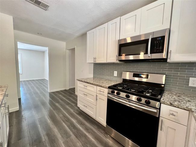Kitchen with appliances with stainless steel finishes, baseboards, backsplash, white cabinets, and dark wood-style floors | Image 9