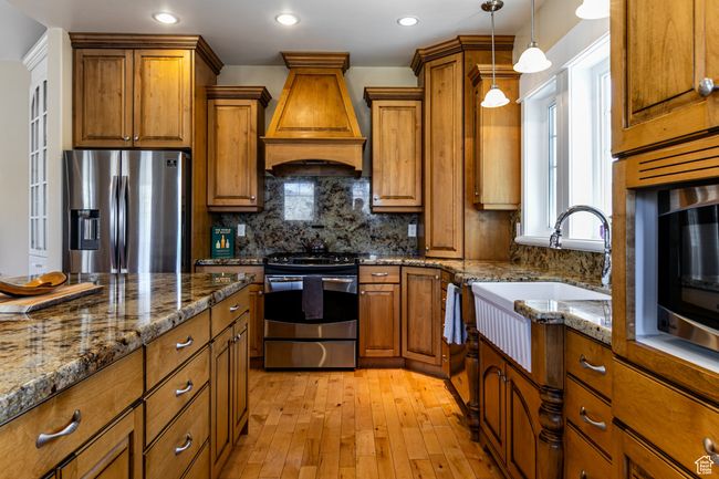 Kitchen with brown cabinets, backsplash, custom range hood, and appliances with stainless steel finishes | Image 7