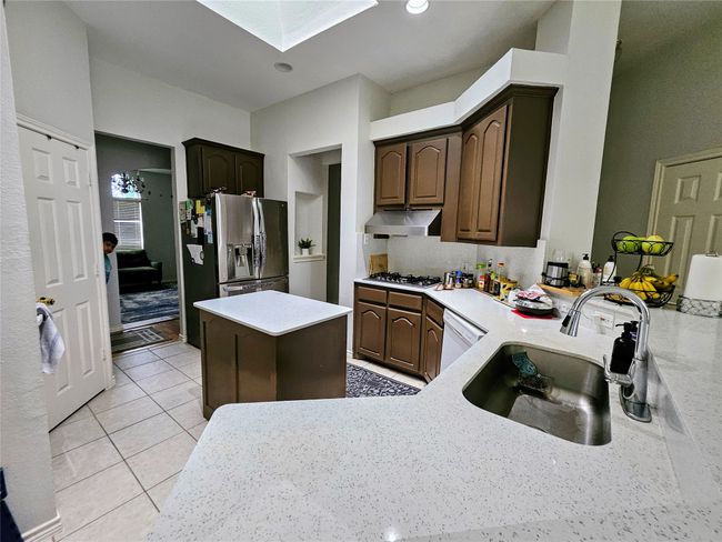 Kitchen featuring extractor fan, appliances with stainless steel finishes, a skylight, light countertops, and a peninsula | Image 9