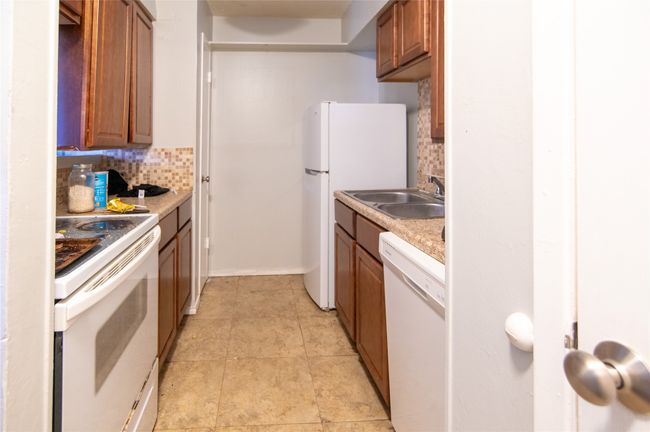 Kitchen featuring white appliances, tasteful backsplash, brown cabinetry, light countertops, and light tile patterned flooring | Image 10