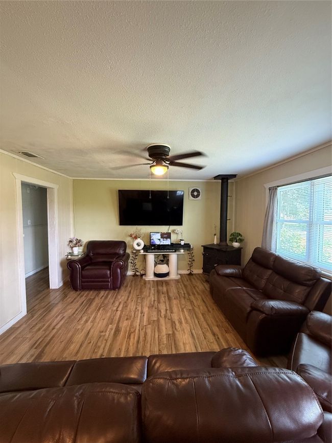 Living area featuring a wood stove, wood finished floors, a textured ceiling, and a ceiling fan | Image 14