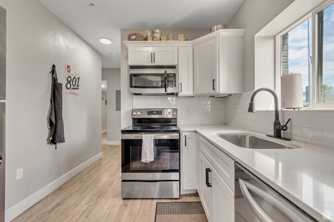 Kitchen with stainless steel appliances, backsplash, white cabinets, light wood finished floors, and light stone counters | Image 7
