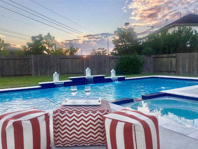 Charming backyard featuring a spacious pool with elegant water features, surrounded by a privacy fence. Enjoy outdoor relaxation with stylish seating and a picturesque sunset view. | Image 6