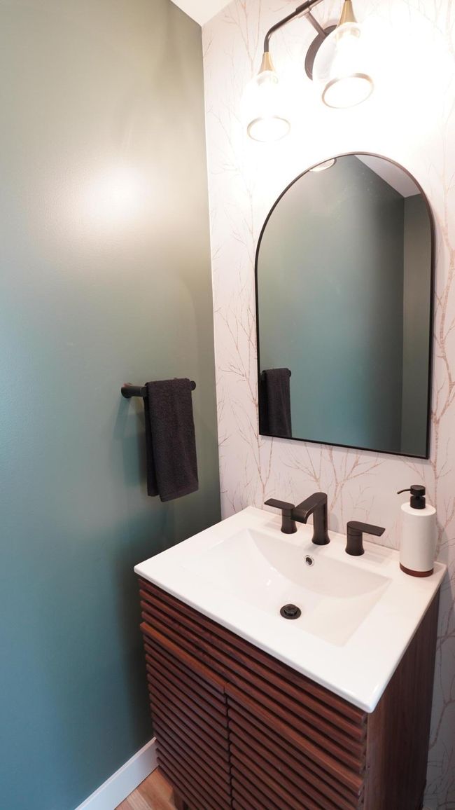 The newly added main level powder room is both bold and inviting with hardwood floors, dark green paint, accent wallpaper and a modern vanity. | Image 37