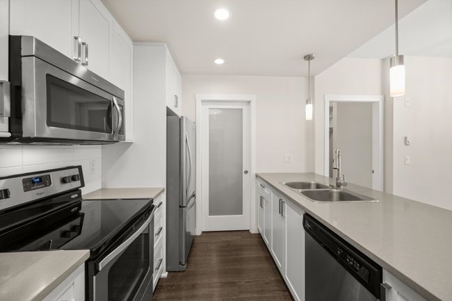 Kitchen featuring appliances with stainless steel finishes, dark wood-style flooring, recessed lighting, decorative light fixtures, and white cabinets | Image 12
