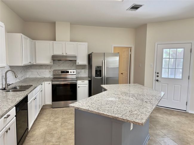 Kitchen featuring stainless steel appliances, decorative backsplash, a center island, light stone countertops, and white cabinetry | Image 5
