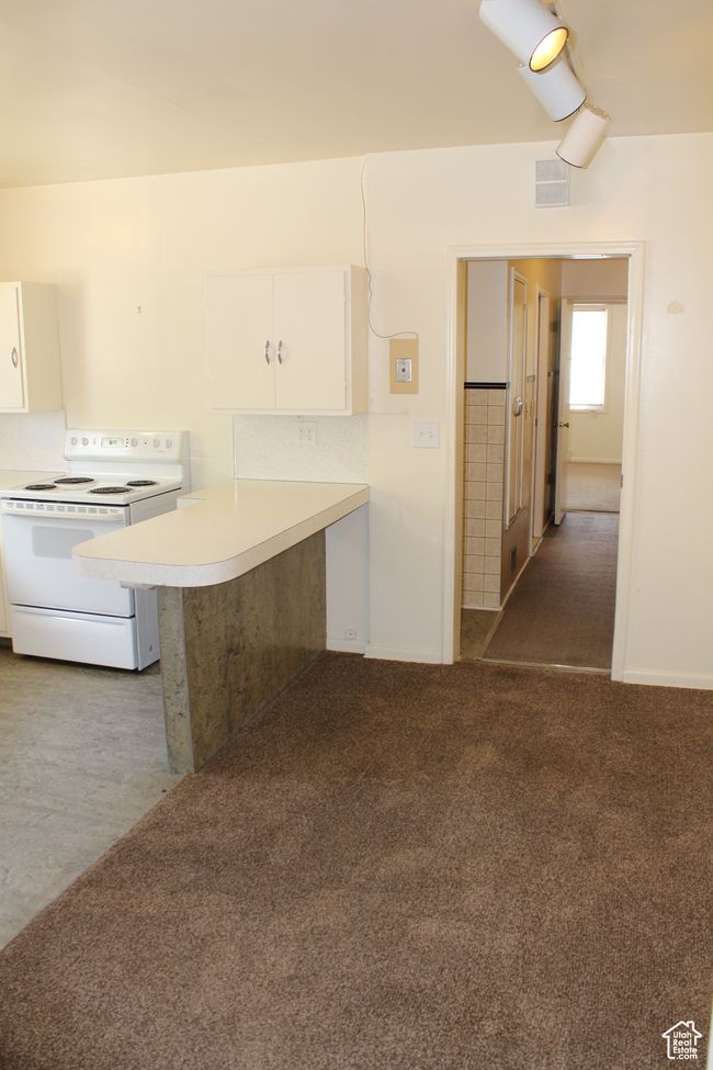 Kitchen with white electric stove, white cabinetry, light countertops, a peninsula, and carpet | Image 30