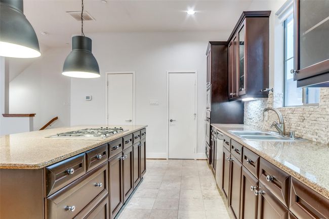 Kitchen with a sink, glass insert cabinets, stainless steel gas cooktop, and backsplash | Image 7