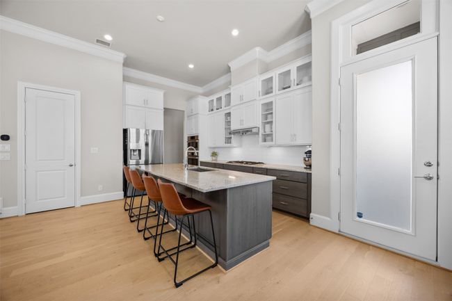 Kitchen with stainless steel appliances, ornamental molding, a kitchen bar, white cabinets, and a center island with sink | Image 7