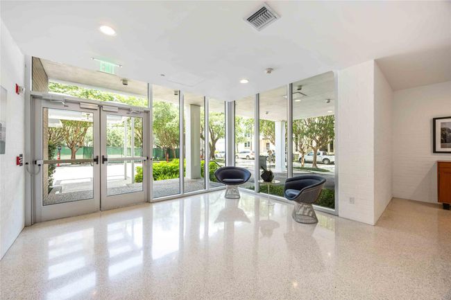 Bright and modern lobby with large glass windows, polished floors, and contemporary seating. The space offers a welcoming view of lush greenery outside. | Image 20