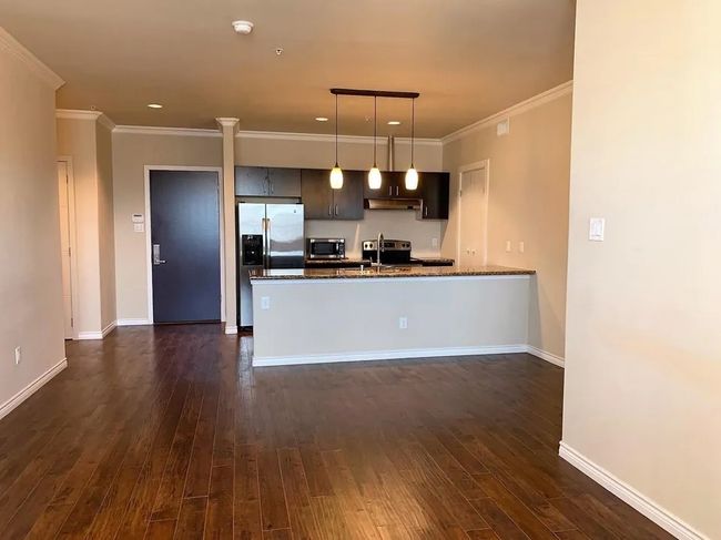 Kitchen with appliances with stainless steel finishes, under cabinet range hood, dark wood-style flooring, ornamental molding, and decorative light fixtures | Image 19