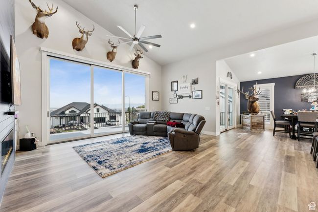 Living room featuring a glass covered fireplace, recessed lighting, light wood finished floors, high vaulted ceiling, and ceiling fan with notable chandelier | Image 47