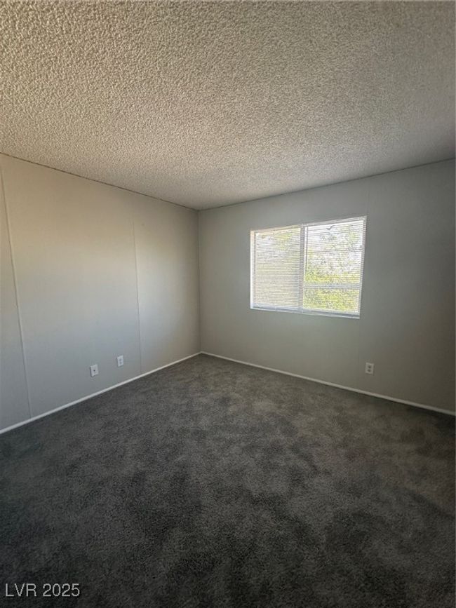 Empty room with dark carpet, a textured ceiling, and baseboards | Image 10