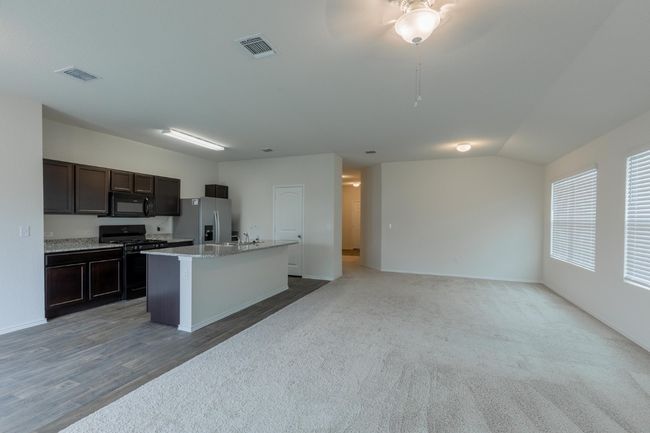 Kitchen with black appliances, a kitchen island with sink, open floor plan, dark brown cabinets, and baseboards | Image 4