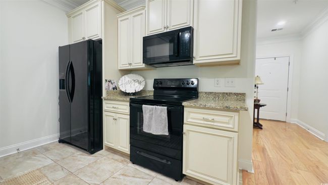 Kitchen with black appliances, crown molding, light stone counters, cream cabinets, and light wood-style flooring | Image 19