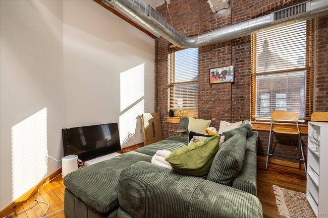 A stylish loft-style interior with exposed brick walls, high ceilings with industrial ductwork, polished hardwood floors, rustic wood doors, and a cozy open layout featuring large windows that bring in natural light | Image 5