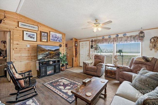 Living area featuring wooden walls, lofted ceiling, a glass covered fireplace, ceiling fan, and a textured ceiling | Image 16
