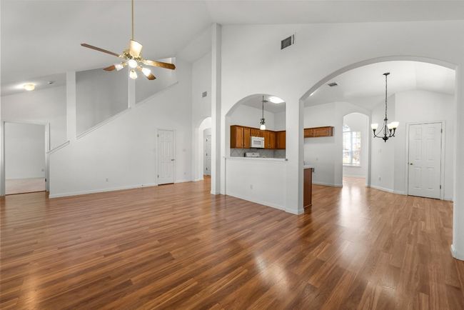 Unfurnished living room featuring wood finished floors, visible vents, baseboards, lofted ceiling, and ceiling fan with notable chandelier | Image 6
