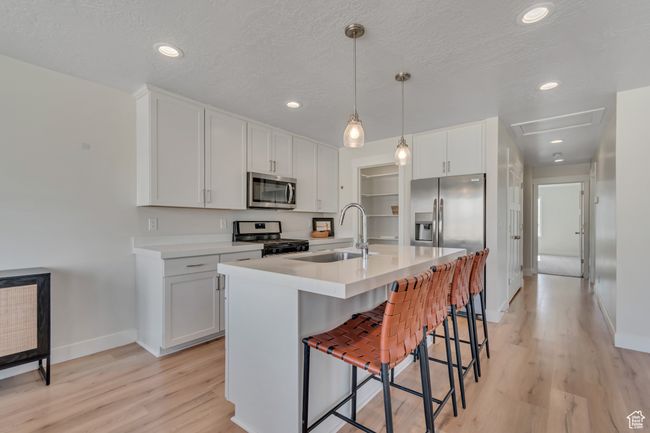 Kitchen featuring stainless steel microwave, range with gas cooktop, a breakfast bar, light wood-type flooring, and light countertops | Image 8