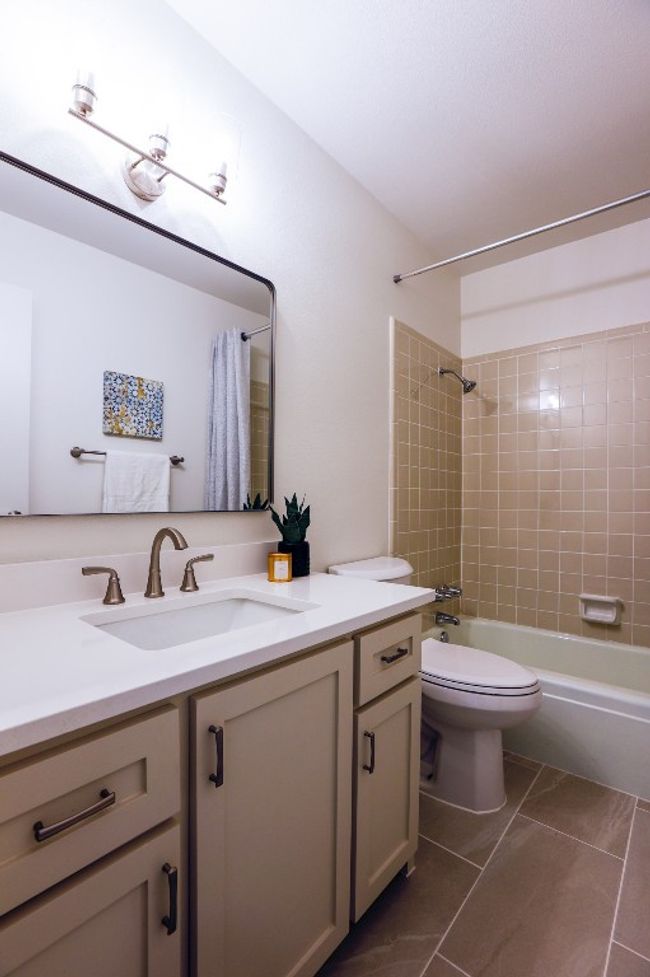 Bathroom featuring custom vanity, shower / bathtub combination with curtain, and marble look tile flooring. | Image 26