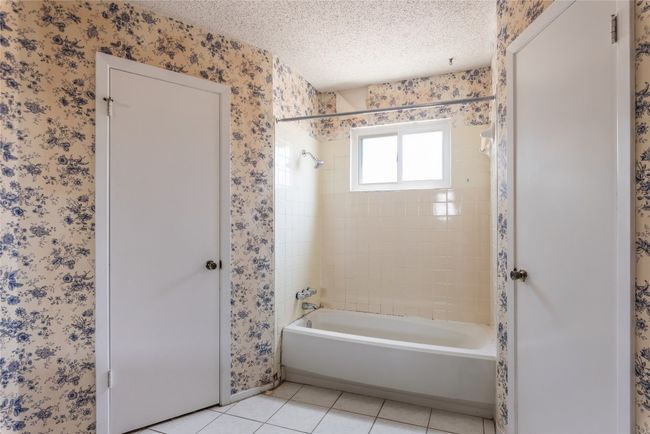 Full bath featuring wallpapered walls, shower combination, tile patterned flooring, a textured ceiling, and baseboards | Image 16