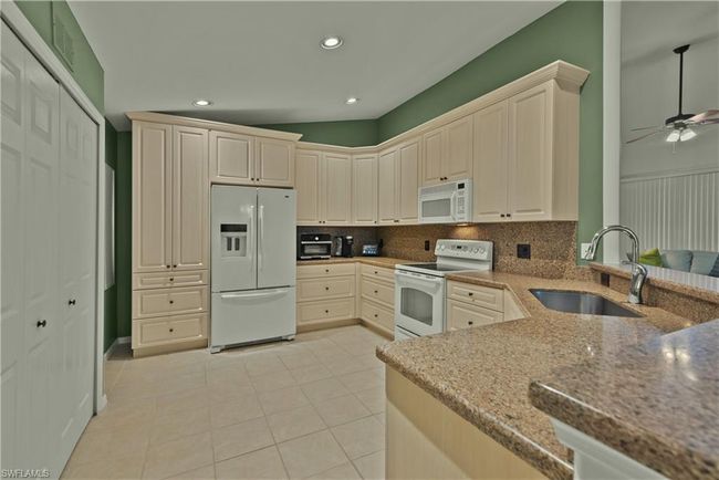 Kitchen with decorative backsplash, sink, light tile patterned floors, white appliances, and ceiling fan | Image 4
